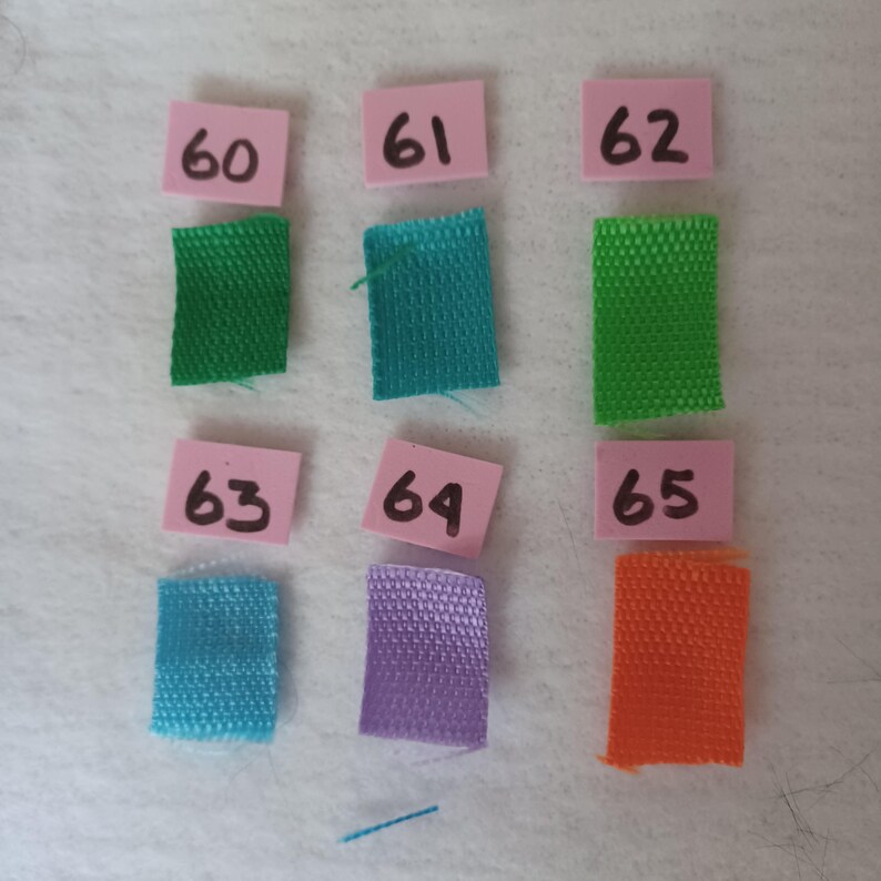 Puede incluir: Seis muestras de tela rectangulares en verde, verde azulado, verde lima, azul claro, morado y naranja, cada una emparejada con una peque&ntilde;a etiqueta cuadrada rosa con los n&uacute;meros 60, 61, 62, 63, 64 y 65 escritos a mano, dispuestos en dos filas.