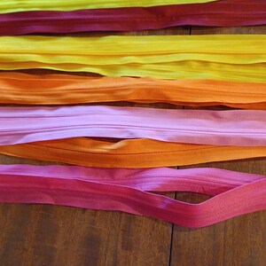 May include: A collection of colorful zippers in shades of yellow, red, orange, and pink, arranged on a wooden surface. The zippers are neatly laid out, showcasing their vibrant hues and potential for craft projects.