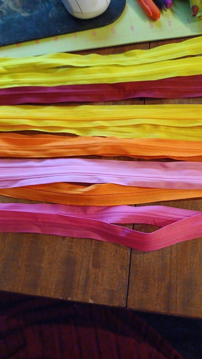 May include: A collection of colorful zippers in shades of yellow, red, orange, and pink, arranged on a wooden surface. The zippers are neatly laid out, showcasing their vibrant hues and potential for craft projects.