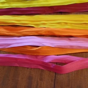 May include: A collection of colorful zippers in shades of yellow, red, orange, and pink, arranged on a wooden surface. The zippers are neatly laid out, showcasing their vibrant hues and smooth texture, ideal for sewing and crafting projects.