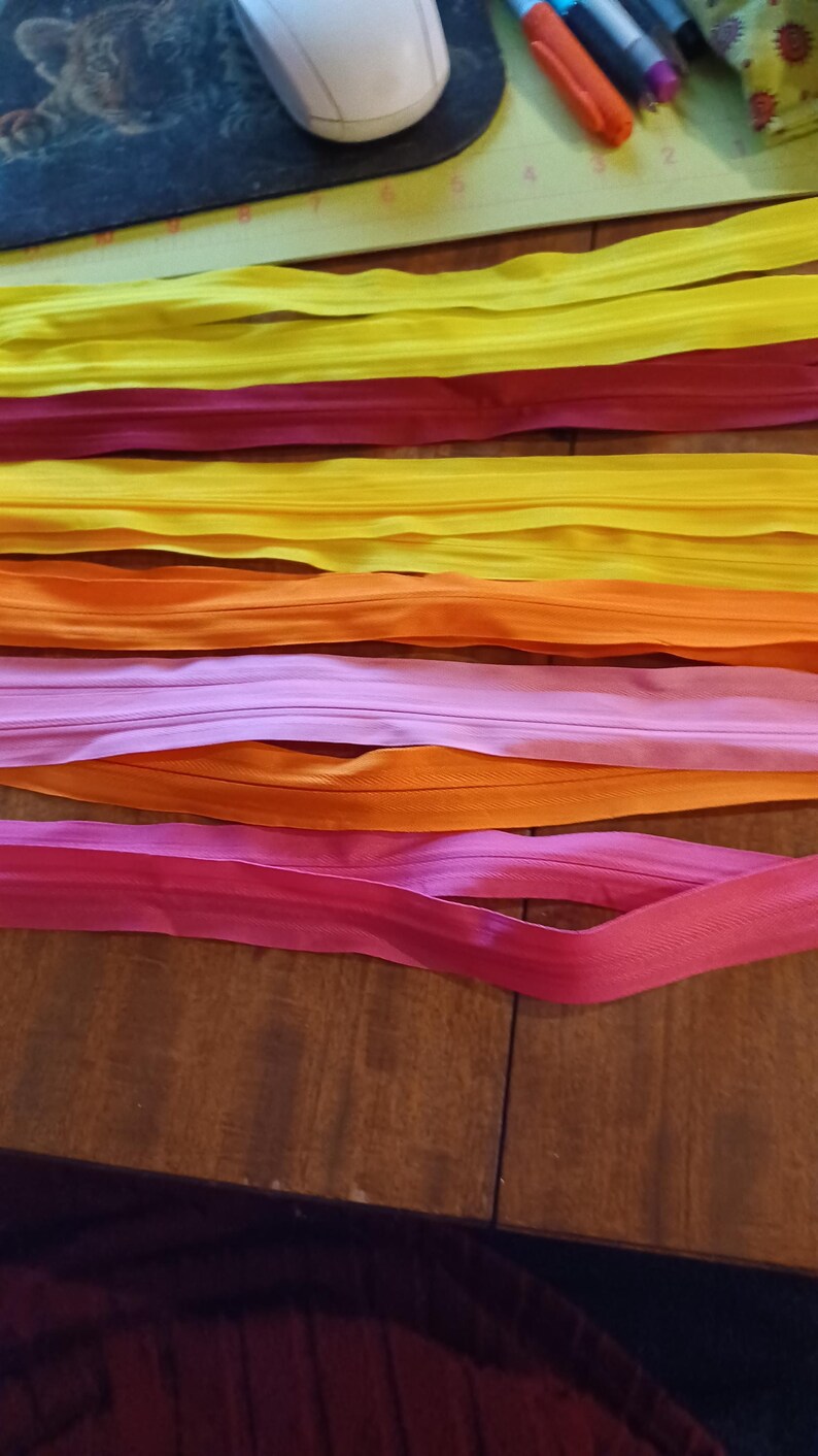 May include: A collection of colorful zippers in shades of yellow, red, orange, and pink, arranged on a wooden surface. The zippers are neatly laid out, showcasing their vibrant hues and smooth texture, ideal for sewing and crafting projects.
