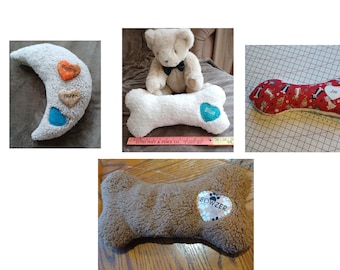Puede incluir: Una colección de almohadas de felpa con forma de hueso de perro y de luna. Las almohadas son de varios colores, incluyendo blanco, marrón y rojo. Algunas almohadas tienen parches en forma de corazón con nombres como "Blue", "Jax" y "Bowzer".
