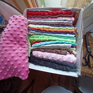May include: A box filled with various colors of dimple dot fabric. A large roll of pink dimple dot fabric is on the left. The box contains folded fabric in red, gray, orange, green, blue, brown, and pink.