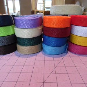 Puede incluir: Una colecci&oacute;n de doce rollos de cinta de nailon tejida dispuestos en cuatro pilas verticales. Los rollos presentan una variedad de colores s&oacute;lidos, incluyendo negro, verde lima, gris oscuro, marr&oacute;n, lavanda, crema, verde oscuro, beige, naranja, granate, azul, rojo, blanco, amarillo y rosa.