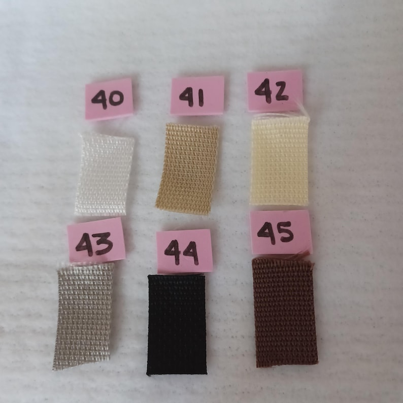 Puede incluir: Seis muestras de tela rectangulares dispuestas en dos filas, etiquetadas con tarjetas de papel rosa numeradas del 40 al 45. Las muestras presentan varios colores s&oacute;lidos, incluyendo blanco, beige, crema, gris claro, negro y marr&oacute;n oscuro.