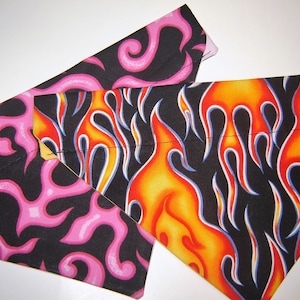 May include: Two fabric dog bandanas with a flame pattern. One bandana is black with pink flames, and the other is black with orange and yellow flames.