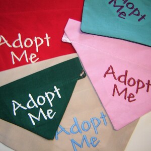 May include: Five dog bandanas with the text "Adopt Me" embroidered on them. The bandanas are in different colors: red, green, pink, blue, and beige.