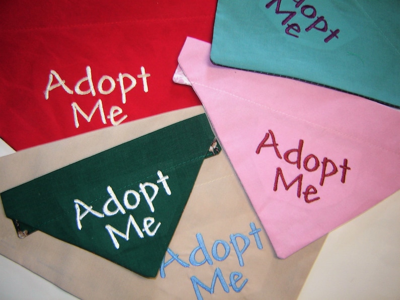 May include: Five dog bandanas with the text "Adopt Me" embroidered on them. The bandanas are in different colors: red, green, pink, blue, and beige.