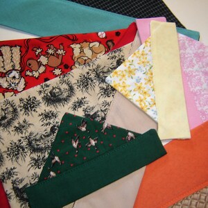 May include: Assortment of fabric scraps in various patterns and colors, including red with dog illustrations, beige with a floral pattern, green with a bird pattern, yellow, pink with a damask pattern, and orange.