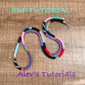 May include: Two beaded necklaces with a variety of colors, including purple, pink, black, and orange. The necklaces are on a wooden surface. The text "PDF TUTORIAL" and "Alev's Tutorials" are written on the image.