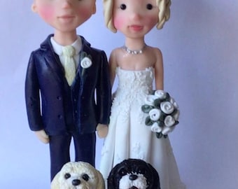 May include: A wedding cake topper featuring a bride and groom in a white dress and blue suit, with two small white dogs with brown and black fur.