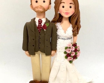 May include: A wedding cake topper featuring a bride and groom figurine. The groom is wearing a brown suit with a red tie and a white shirt. The bride is wearing a white dress with a lace bodice and a bouquet of pink and burgundy roses.