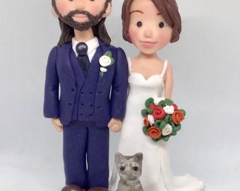 May include: A wedding cake topper featuring a bride and groom in a blue suit and white dress, with a gray cat figurine standing in front of them.