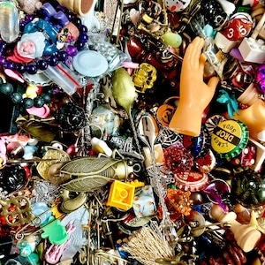 May include: A collection of various small objects, including charms, beads, miniature toys, and decorative elements. The items are in a variety of colors, including gold, silver, red, and blue. There are chess pieces, a plastic hand, and bottle caps.