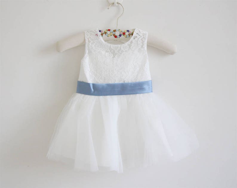 Pu&ograve; includere: Abito in tulle bianco con corpetto in pizzo e una cintura in raso blu chiaro.