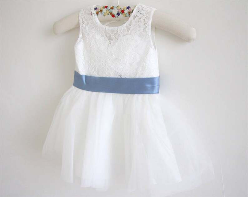Pu&ograve; includere: Abito in tulle bianco con corpetto in pizzo e una cintura in raso blu chiaro.