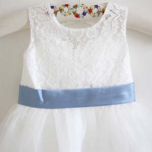 Pu&ograve; includere: Abito bianco senza maniche in pizzo con un nastro di raso blu. L'abito ha una gonna di tulle ed &egrave; perfetto per una damigella d'onore.