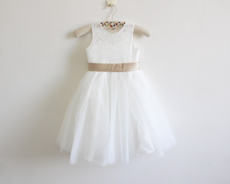 May include: White tulle dress with a lace bodice and a gold satin sash.