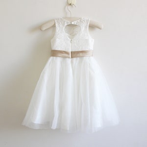 May include: White tulle dress with a lace bodice and a gold satin sash. The dress has a heart-shaped cutout in the back.