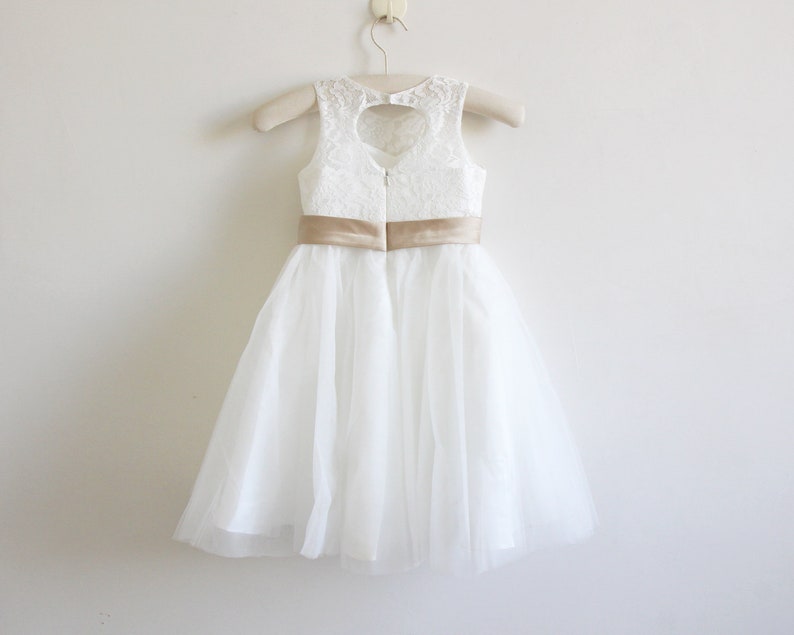 May include: White tulle dress with a lace bodice and a gold satin sash. The dress has a heart-shaped cutout in the back.