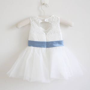Pu&ograve; includere: Abito in tulle bianco con corpetto in pizzo e cintura in raso blu chiaro. L'abito ha uno scollo a forma di cuore sul retro.