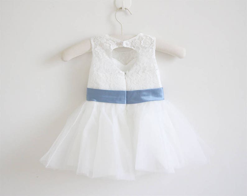 Pu&ograve; includere: Abito in tulle bianco con corpetto in pizzo e cintura in raso blu chiaro. L'abito ha uno scollo a forma di cuore sul retro.