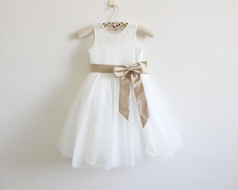 May include: White tulle dress with a lace bodice and a gold satin sash tied in a bow.