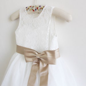 May include: White tulle dress with a lace bodice and a gold satin sash tied in a bow.