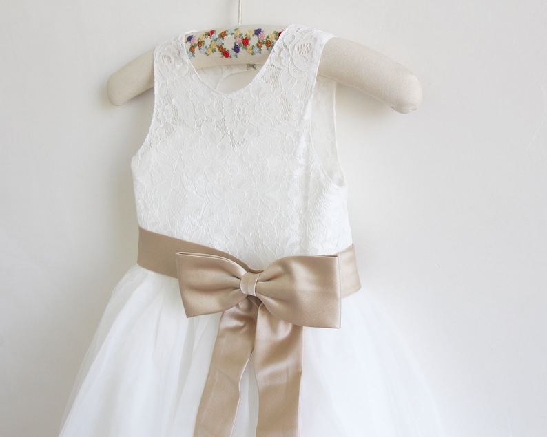May include: White tulle dress with a lace bodice and a gold satin sash tied in a bow.