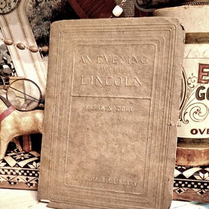 May include: A vintage book titled "An Evening with Lincoln" by Sherwin Cody. The book has a textured, tan cover with embossed lettering and is part of "The Nutshell Library". The image shows the book among other antique items.