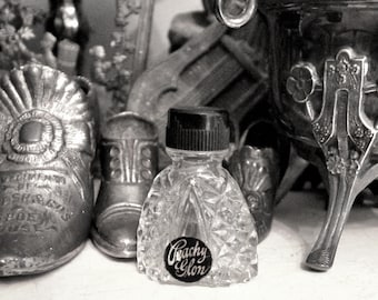 May include: A clear glass bottle with a textured surface and a black cap. The bottle is filled with a clear liquid and has a label that reads "Coachy Glam".
