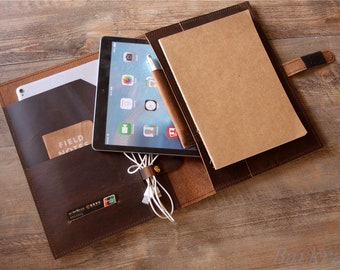 May include: A brown leather portfolio with a flap closure and a strap. The portfolio has a pocket for a tablet, a pen holder, and a pocket for a notebook. The notebook is brown and has the words "FIELD NOTES" printed on the cover.