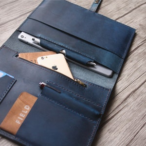 May include: A blue leather folio with multiple pockets and compartments. The folio is open, revealing a smartphone, pen, and cards. The folio has a zipper pocket and a snap closure. The leather has a distressed appearance.