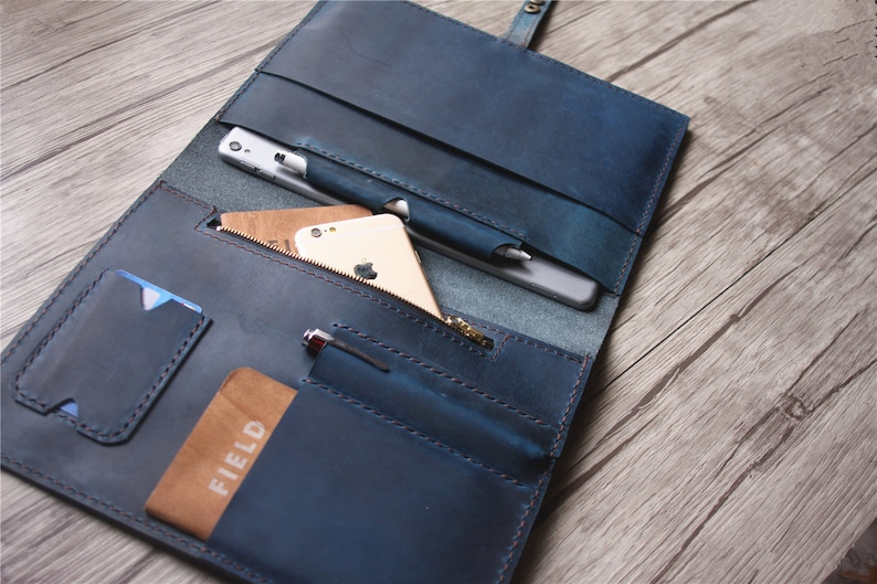 May include: A blue leather folio with multiple pockets and compartments. The folio is open, revealing a smartphone, pen, and cards. The folio has a zipper pocket and a snap closure. The leather has a distressed appearance.