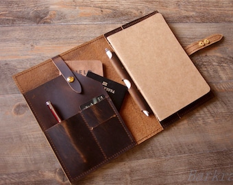 May include: A brown leather journal with a notebook, pen holder, and multiple pockets for cards and other items. The journal has a strap with a brass buckle.