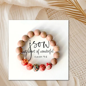 May include: A wooden bracelet with red and white floral beads. The bracelet has the words "j.s.o.w. just short of wonderful ISAIAH 9:6" printed on a white card.