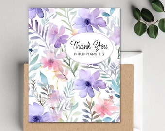 May include: A floral thank you card with a watercolor design. The card features purple and pink flowers with green leaves on a white background. The text "Thank You" is in a white oval, with "Philippians 1:3" below it. The card is paired with a brown envelope.