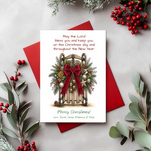 May include: A white Christmas greeting card featuring a wooden sled illustration adorned with pine branches, a large red velvet bow, gold bells, and dried orange slices. The text reads: May the Lord bless you and keep you on this Christmas day and throughout the New Year. Merry Christmas! Love, David, Sarah, Mckenna & Bella.
