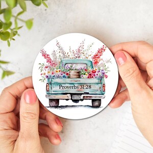 May include: A teal blue pickup truck with a white wooden bed filled with colorful flowers. The truck has the words "Proverbs 31:28" printed on the back.