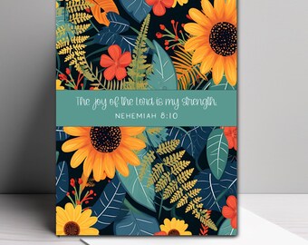 May include: A rectangular greeting card featuring a dark background with yellow sunflowers, red flowers, and green fern leaves. A horizontal teal band across the center displays the white text: The joy of the Lord is my strength. NEHEMIAH 8:10.