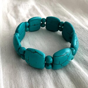 May include: A turquoise blue stretchy bracelet made of square-shaped beads.