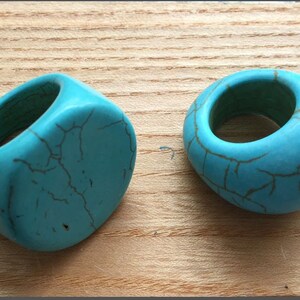 May include: Two turquoise rings made of stone with a crackled finish. The rings are different shapes, one is round and the other is oval.