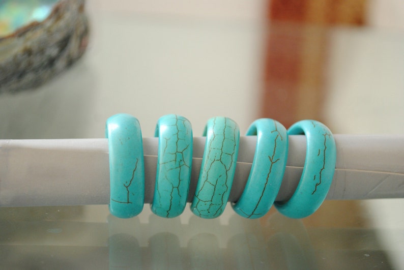 May include: Five turquoise rings with a marbled pattern, stacked on a white surface.