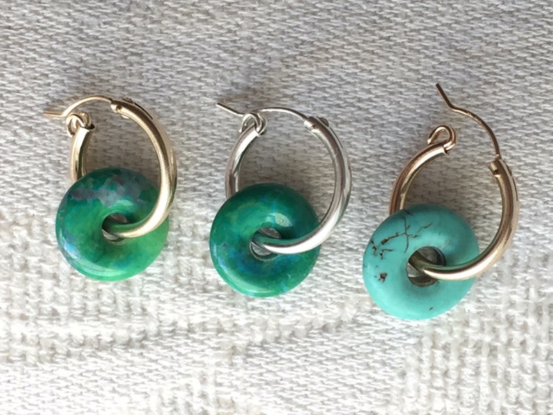 May include: Three pairs of hoop earrings with turquoise and green stone accents. The hoops are made of gold and silver metal.