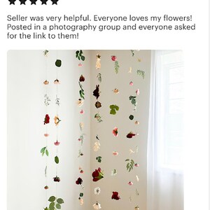 May include: Multiple vertical strands of hanging flowers and green leaves suspended from above. The arrangement features various floral blooms in shades of red, pink, white, and cream, interspersed with green foliage along thin, clear strings.