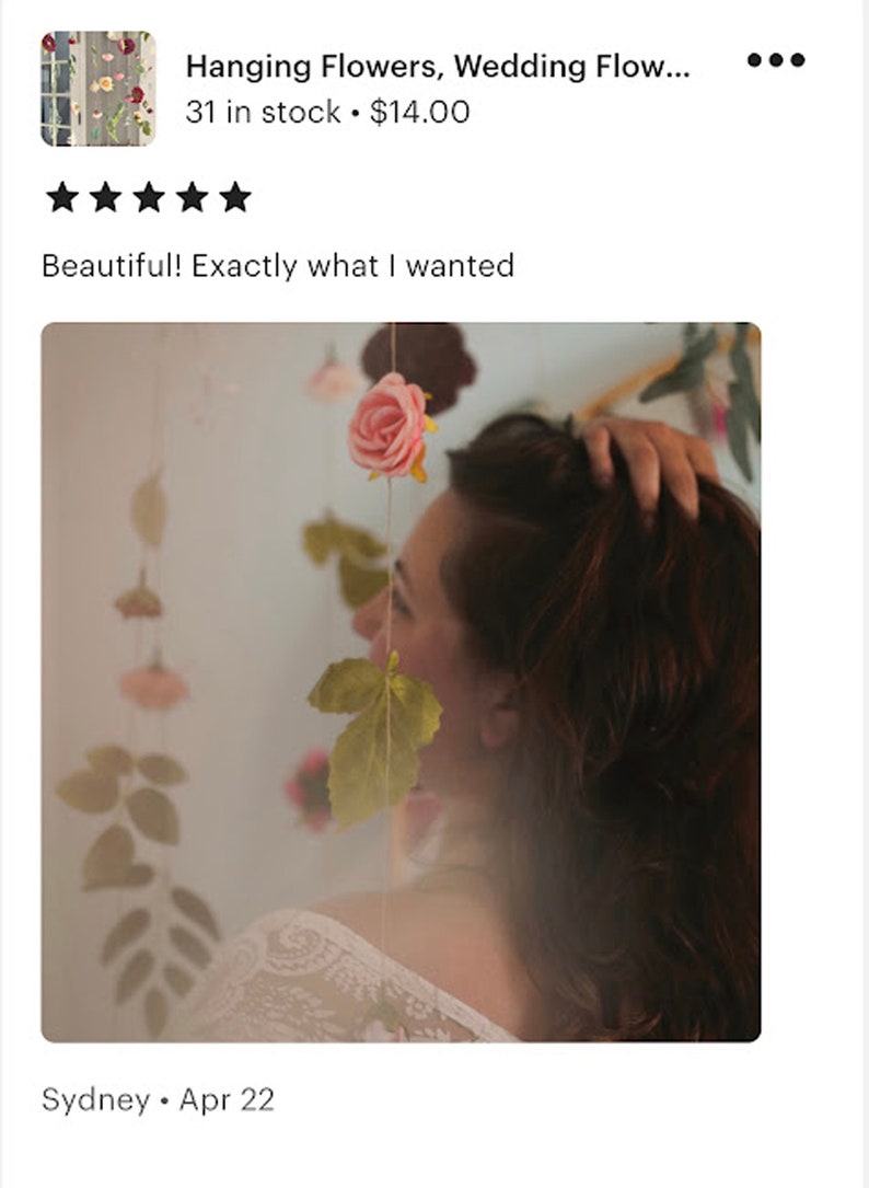 May include: A vertical string of artificial flowers featuring a soft pink rose at the top, followed by green leaves and additional small floral elements suspended on a thin cord. The arrangement is designed to hang vertically as a decorative piece.