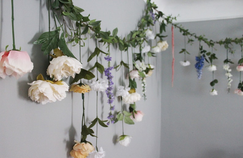 Pu&ograve; includere: Una ghirlanda floreale con fiori appesi nei toni del bianco, rosa, giallo e viola. La ghirlanda &egrave; composta da fiori e verde artificiali, creando un'esposizione decorativa. I fiori sono attaccati a un tralcio.