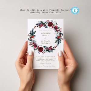 May include: A rectangular wedding invitation card featuring a central wreath of dark red roses, green pine needles, and red berries. The text reads Meagan Jones and Michael Thomas, with event details including December 21, 20xx, at Marriott Carlton Hotel.