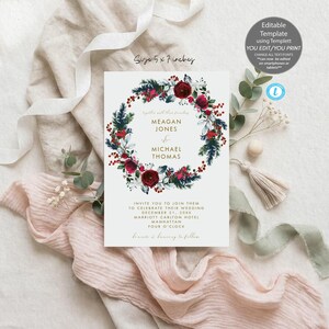 May include: A 5 by 7 inch wedding invitation card featuring a central wreath of dark red roses, pine needles, and red berries. The text reads Meagan Jones and Michael Thomas, invite you to join them to celebrate their wedding December 21, 20XX.