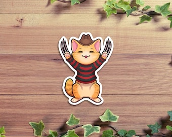 May include: A cute orange cat wearing a red and black striped shirt and a brown cowboy hat. The cat has black claws and is smiling.